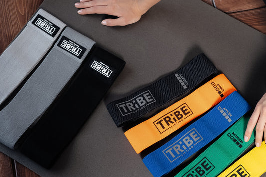Tribe Lifting gray 3-pack and multicolor 5-pack fabric resistance bands displayed on an exercise mat for tension level comparison.