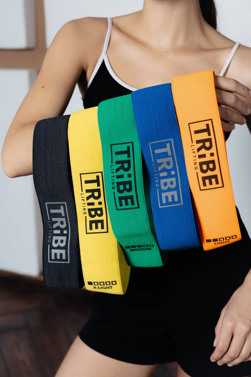 Woman holding five Tribe Lifting fabric resistance bands in different resistance levels