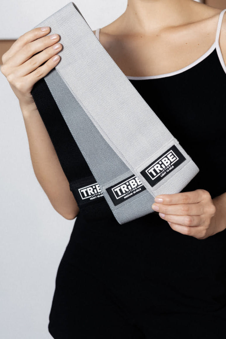 Woman holding three Tribe Lifting gray fabric resistance bands in different resistance levels